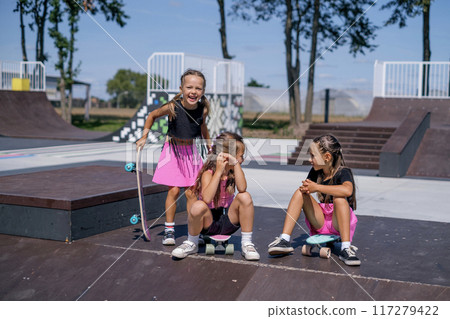 Hilarious funny girls with skateboards are sitting on the fun boxes pyramids of skate park Hilarious funny girls with skateboards are sitting on the fun boxes pyramids of skate park 117279422