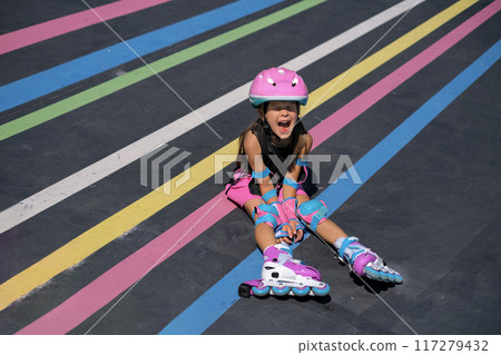 A hysterical girl screams while sitting on the track of a roller rink after falling from roller skates 117279432