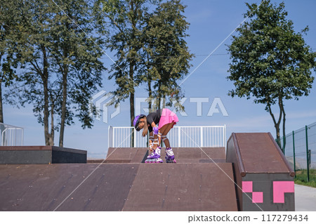 A girl on roller skates stands at the top of the skate park ramp, adjusting the rollers 117279434