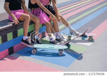 Three Girls are sitting on a skatepark bench with skates, close-up 117279436