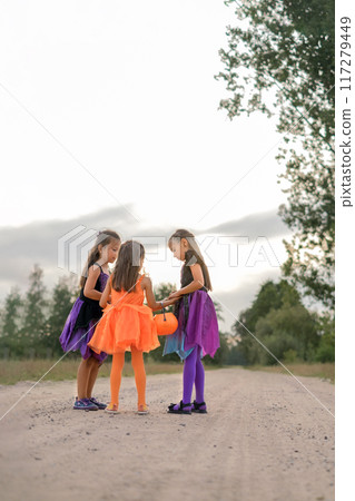 Girls in Halloween witch costumes are chatting in the middle of a sandy street with a bucket in the shape of a pumpkin Girls in Halloween witch costumes are chatting in the middle of a sandy street with a bucket in the shape of a pumpkin 117279449