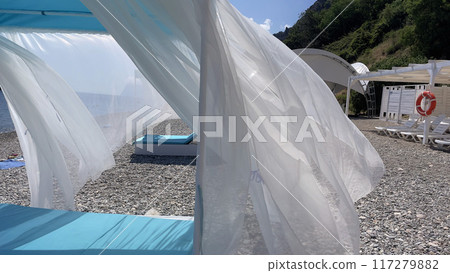 A beach scene with a white tent and blue umbrella 117279882