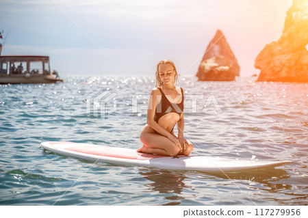 Woman sup sea. Sports girl on a surfboard in the sea on a sunny summer day. In a black bathing suit, he sits on a sapa in the sea. Rest on the sea. 117279956