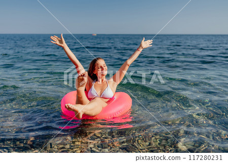 A woman is floating on a pink inflatable raft in the ocean A woman is floating on a pink inflatable raft in the ocean 117280231