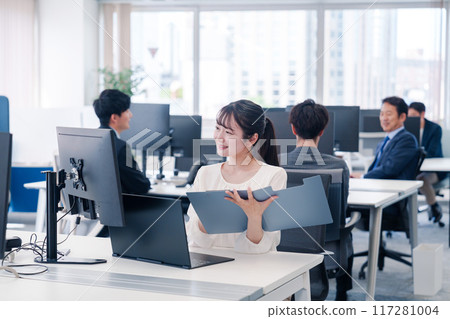 一位年輕女子在辦公室的辦公桌前微笑著工作 一位年輕女子在辦公室的辦公桌前微笑著工作 117281004