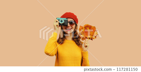 Autumn color style outfit, stylish young woman photographer with camera holds yellow maple leaves Autumn color style outfit, stylish young woman photographer with camera holds yellow maple leaves 117281150