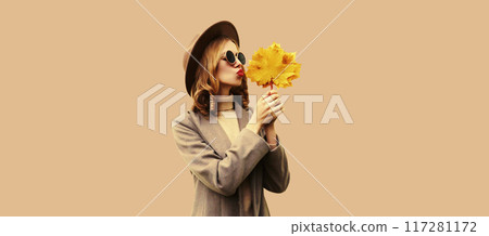 Autumn color style outfit, beautiful young woman with yellow maple leaves wearing round hat, coat Autumn color style outfit, beautiful young woman with yellow maple leaves wearing round hat, coat 117281172