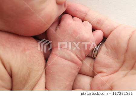 Close-up little hand of child and palm of mother and father. The newborn baby has a firm grip on the parent's finger after birth. A newborn holds on to mom's, dad's finger.  117281551