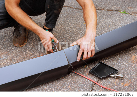 When aluminum rain gutters have been bent on machine tool, worker cuts them to required size with shears When aluminum rain gutters have been bent on machine tool, worker cuts them to required size with shears 117281862