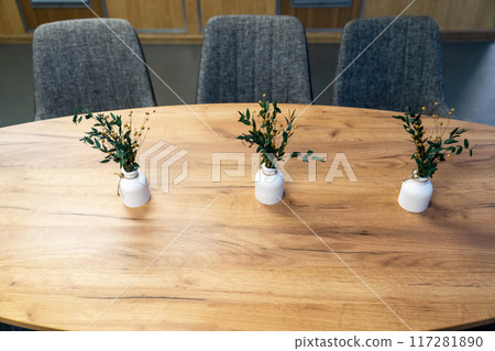 Three vases with greenery placed on a wooden table in an indoor setting 117281890