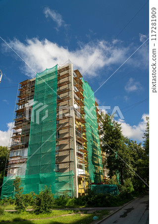 A tall building is under renovation with green netting covering its sides A tall building is under renovation with green netting covering its sides 117281909