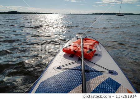 Paddleboard resting on water with a life vest beside it 117281934