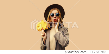 Autumn portrait of emotional young woman surprised by the low prices holds yellow maple leaves 117281983