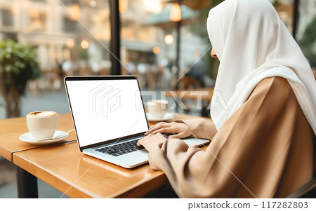 Arab woman in hijab using blank screen laptop in cafe or coworking space, remote work concept 117282803
