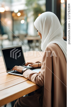 Arab woman in hijab using blank screen laptop in cafe or coworking space, remote work concept 117282804