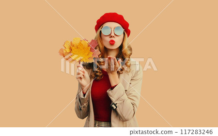 Autumn portrait of stylish beautiful woman with yellow maple leaves blowing kiss in red french beret 117283246