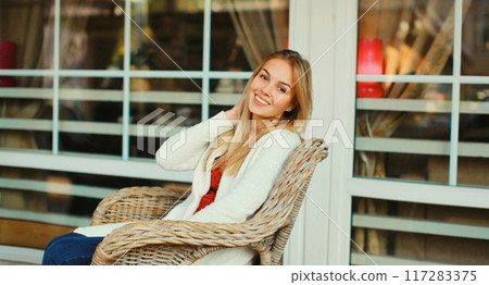 Portrait of beautiful blonde smiling young woman sitting on chair waiting in city cafe 117283375