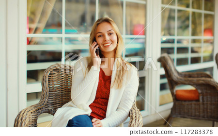 beautiful blonde smiling young woman calling on mobile phone sitting on chair waiting in city cafe beautiful blonde smiling young woman calling on mobile phone sitting on chair waiting in city cafe 117283378