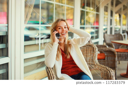 beautiful blonde smiling young woman calling on mobile phone sitting on chair waiting in city cafe 117283379