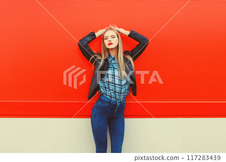 Fashion portrait of beautiful blonde young woman posing in black leather jacket on red background Fashion portrait of beautiful blonde young woman posing in black leather jacket on red background 117283439