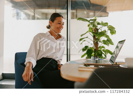 A Professional Woman is in a Modern Workspace while Actively Engaged in an Online Meeting 117284332