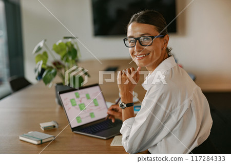 A Smiling Professional Woman Engaged in Her Work on a Laptop Inside a Modern Office Space A Smiling Professional Woman Engaged in Her Work on a Laptop Inside a Modern Office Space 117284333