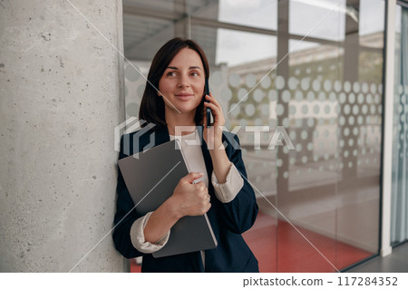A professional businesswoman with phone and portfolio in a modern office building A professional businesswoman with phone and portfolio in a modern office building 117284352