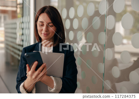 A businesswoman is shown multitasking by using a smartphone along with a tablet 117284375