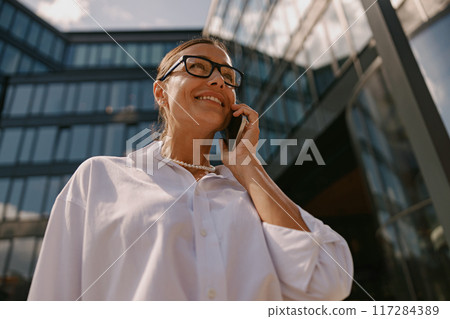 A focused businesswoman is engaged in an important call outside a modern office building 117284389