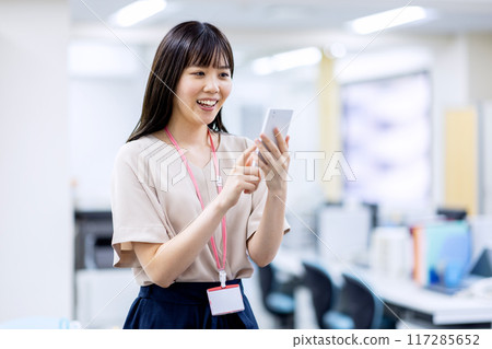 一個二十多歲的女人在辦公室裡操作智能手機 一個二十多歲的女人在辦公室裡操作智能手機 117285652