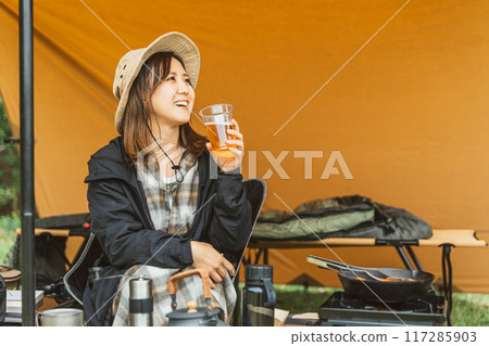 Young female camper (drinking) camping solo at campsite Young female camper (drinking) camping solo at campsite 117285903