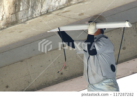 Electrical work: Workers installing lighting fixtures on the ceiling of the staircase 117287282