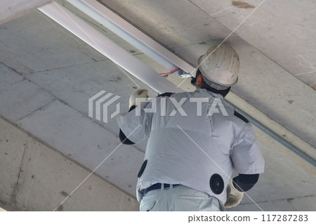 Electrical work: Workers installing lighting fixtures on the ceiling of the staircase 117287283