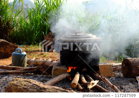 A outdoor steaming black pot on open fire on makeshift stove made of bricks and stones, surrounded by nature, as traditional Vietnamese cook banh tet for Tet holiday is culture culinary 117287509