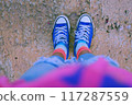 classic blue sneakers with worn white laces, resting concrete ground, shoes with colorful socks. Woman standing to waiting or thinking moment of carefree youth in urban style 117287559