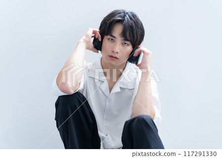 Young man listening to music through headphones 117291330