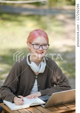 Young woman with a laptop and notes studying in the park for education in nature to relax and learn online. 117292266