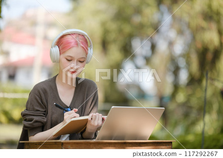 Young woman with a laptop and notes studying in the park for education in nature to relax and learn online. 117292267