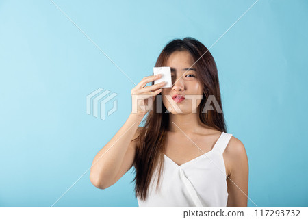 Facial Beauty Treatment Hygiene skin. Asian beautiful young woman removing cosmetic make up using pad cotton face cleaner disc, studio shot isolated on blue background, Happy female cleaning eyes Facial Beauty Treatment Hygiene skin. Asian beautiful young woman removing cosmetic make up using pad cotton face cleaner disc, studio shot isolated on blue background, Happy female cleaning eyes 117293732