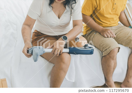 Asian couple with prosthetic leg sitting in living room Asian couple with prosthetic leg sitting in living room 117295670