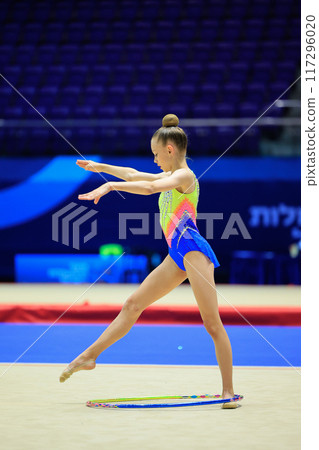 A young gymnast displays dedication, determination, and grace with a hoop in a lively competition 117296020