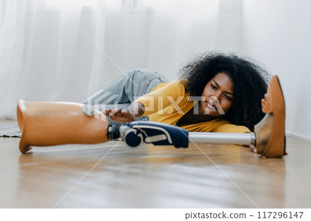 Woman with trying catch prosthetic leg on floor 117296147