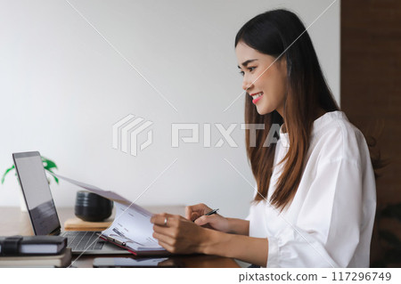 Businesswomen reading data on laptop and checking finance document while working in outside office 117296749