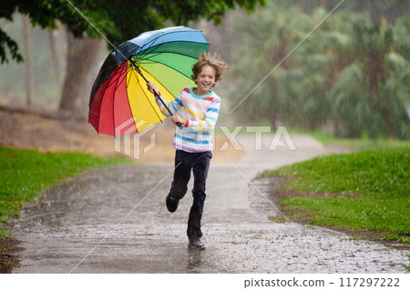 Child playing in rain. Kid jumping in puddle. 117297222