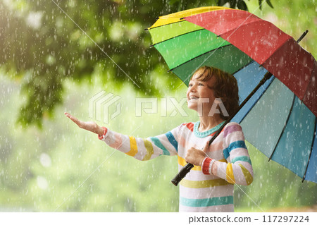 Child playing in rain. Kid jumping in puddle. 117297224