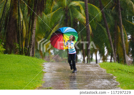 Child playing in rain. Kid jumping in puddle. 117297229