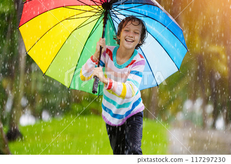 Child playing in rain. Kid jumping in puddle. 117297230