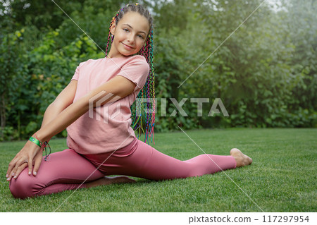 Smiling young girl is performing gymnastic exercises outside. Smiling young girl is performing gymnastic exercises outside. 117297954