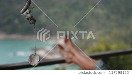 Sea shells and corals swaying on the wind. Woman barefoot legs in background, close up seashells strung on a rope sway in the wind by the sea. Relaxation, silence and tranquility. Slow Sea shells and corals swaying on the wind. Woman barefoot legs in background, close up seashells strung on a rope sway in the wind by the sea. Relaxation, silence and tranquility. Slow 117298153