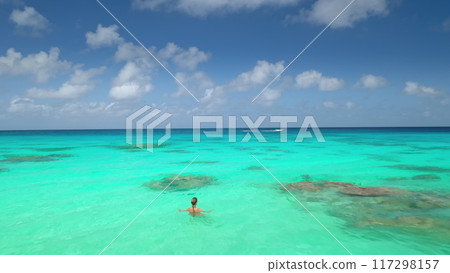 Woman swimming in crystal turquoise sea water under blue clouds sky in sunny day. Tourist girl relax and enjoy outdoor lifestyle travel on summer holiday vacation. Aerial view drone 117298157